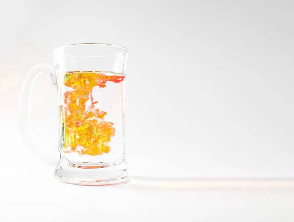 黄色のインクで覆われた水のガラスは 渦巻きとねじれ 白の上に隔離されたガラスのマグカップで スタジオの写真撮影 化学や科学実験の概念 — ストック写真