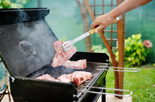 Man at a barbecue grill preparing meat for a garden party — Stock Photo, Image