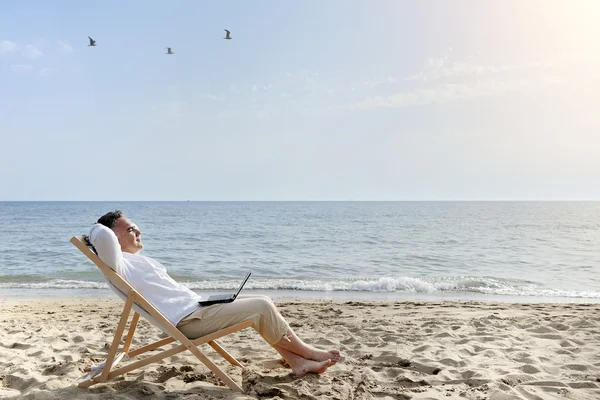 Человек с ноутбуком компьютер отдыхает на пляже — стоковое фото