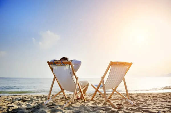 Man avkopplande på stranden sitter på solstol — Stockfoto