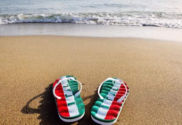 Chanclas con la palabra Italia en arena de playa - vacaciones y concepto de relajación —  Fotos de Stock