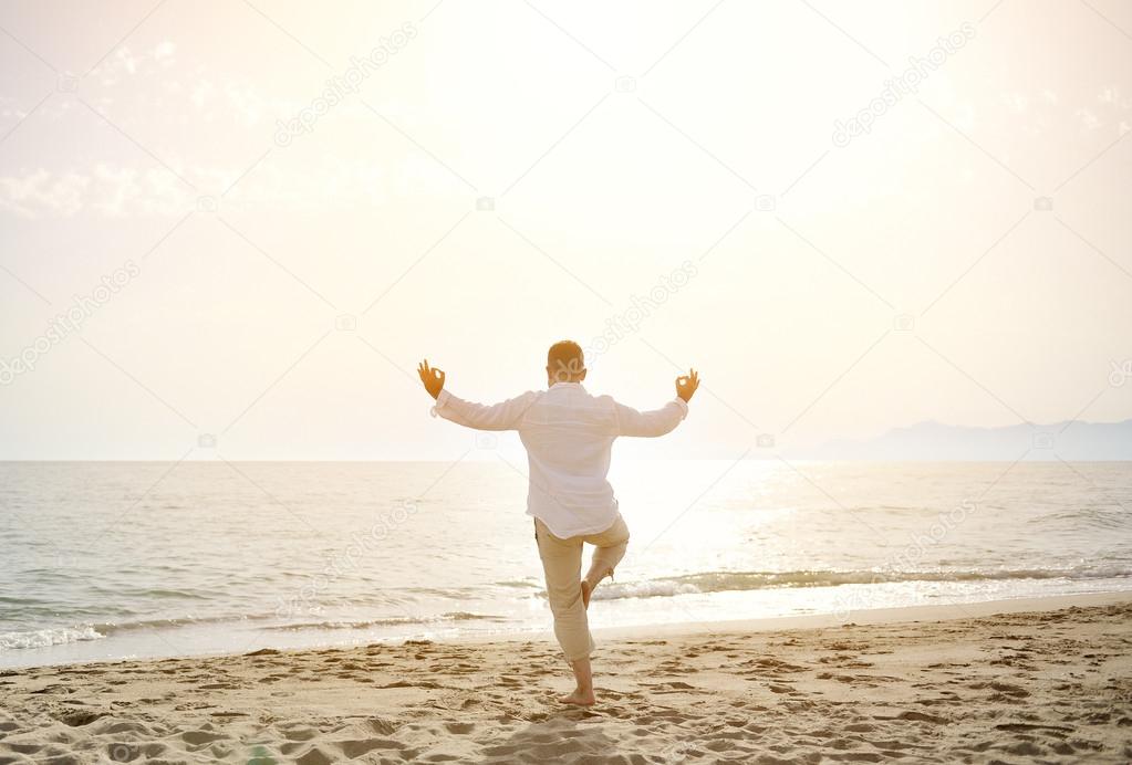 man doing yoga exercises on the beach - healthy lifestyle concept