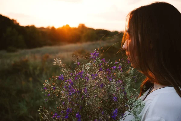 Ekoterapinin Yararları, Doğa Etkisi Refahının İyileştirme Gücü. Uzun saçlı ve bir buket kır çiçekli mutlu genç kadın gün batımında hayatın ve doğanın tadını çıkar.