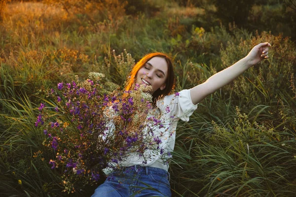 Läkande effekt av, Fördelar med Ecotherapy, Nature Impact Wellbeing. Lycklig ung kvinna med långt hår och en bukett vilda blommor njuta av naturen och livet vid solnedgången — Stockfoto