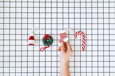 Noel Örgü Oyuncakları. El yapımı DIY Crochet şapkası, lolipop, donut, çorap ve beyaz arka planda dişi eli. Noel örgü desenleri. Özel bütçeli Noel hediyeleri