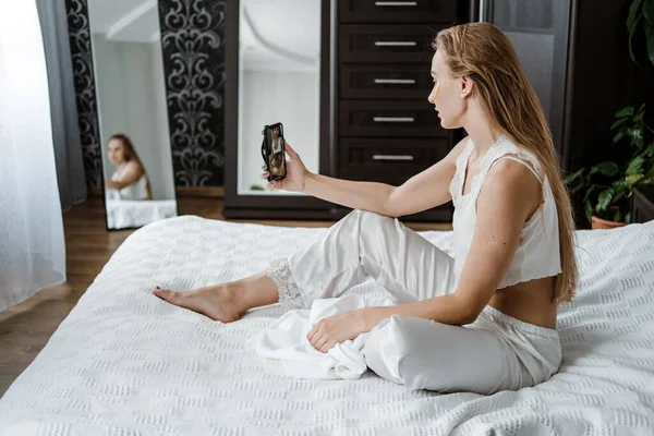 Belleza blogger, vlogger, influencer, redes sociales. Mujer joven en pijama, toalla en la cabeza y con manchas de colágeno cosmético bajo los ojos charlando en el teléfono celular. — Foto de Stock