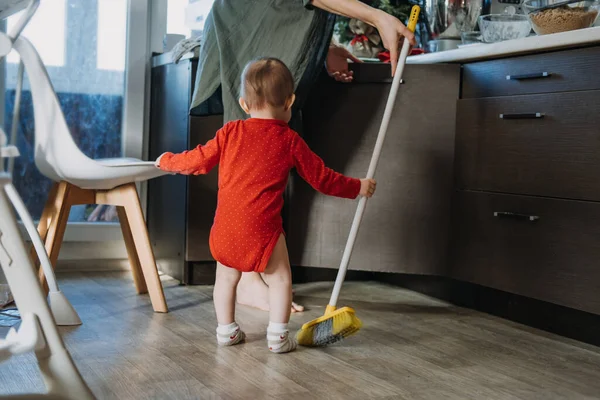 Kleine Mütter helfen. Nettes kleines Mädchen mit Wischmopp hilft ihrer Mutter bei der Hausarbeit in der Küche. Nettes kleines Mädchen spielt mit Wischmopp und putzt das Haus — Stockfoto
