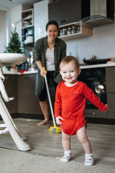Little mothers helper. Cute toddler baby girl with mop help her mom do housework in kitchen. Cute little baby girl play with mop and makes cleaning the house — Stock Photo, Image