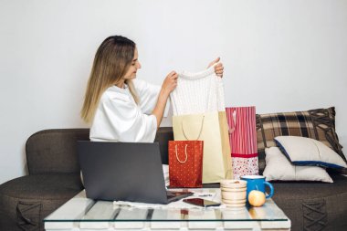 Kara Cuma, online satış, internet alışverişi, ecommerce. Beyaz bir kadın alışveriş çantasından evdeki laptop 'dan yeni kıyafetler çıkarıyor. Kadınlar hafta sonu evde alışveriş yapmayı severler.