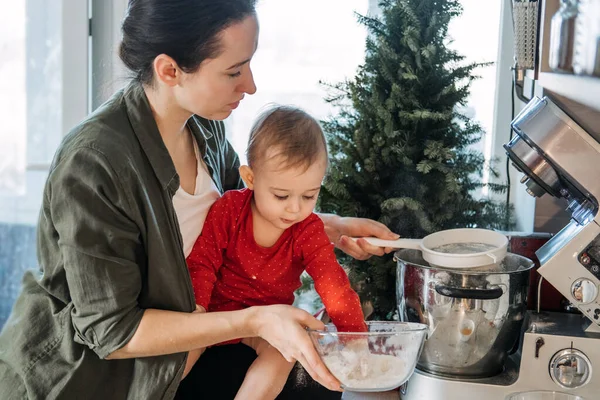 Cozy Christmas at home. Family preparation holiday dessert. Mother and baby toddler daughter play together and cooking gingerbread on kitchen — Stock Photo, Image