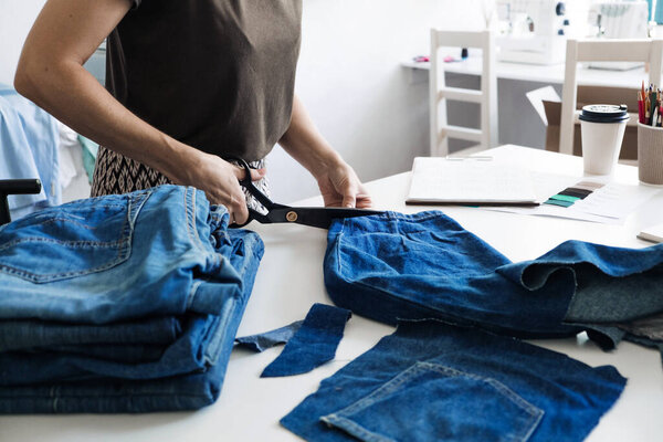 Denim Upcycling Ideas, Using Old Jeans, Repurposing Jeans, Reusing Old Jeans, Upcycling Stuff. Женщина-швея стрижет и ремонтирует старые синие джинсы в швейной мастерской.