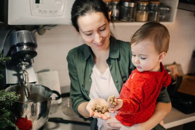 Evde sıcak bir Noel. Aile hazırlığı bayram tatlısı. Anne ve bebek bebek kız un ile oynuyor, hamur yapıyor ve evde mutfakta zencefilli ekmek pişiriyorlar..
