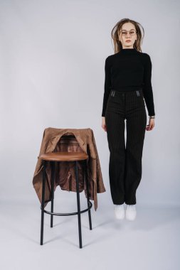 Genç bir kadın, moda tasarımcısı, tam boy günlük tarz portresi. Siyah balıkçı yaka ve bar taburesi giyen şık bir kadın. Uzun saçlı, günlük kıyafetlerle şık sarışın kızın stüdyo fotoğrafı..