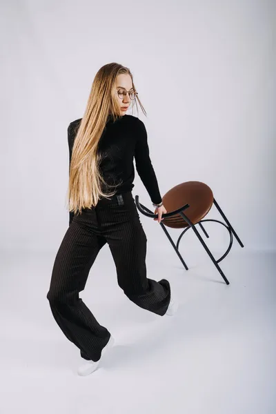 Młoda kobieta, projektantka mody, stylistka portret w stylu casual. Modna kobieta w czarnym golfie i stołku barowym. Studio shot stylowej blondynki z długimi włosami w ubraniach casual. — Zdjęcie stockowe