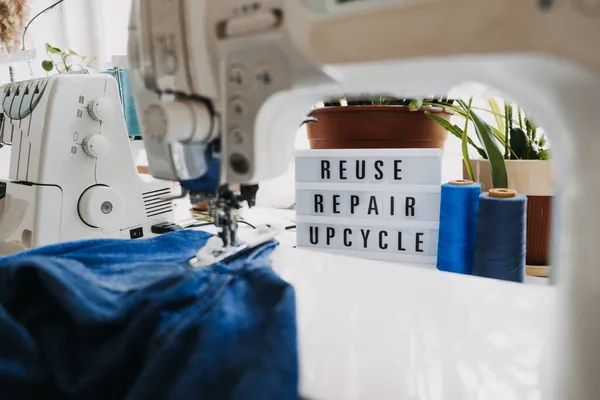 Reutilização, reparação, upcycle texto em placa de luz no fundo máquinas de costura. Pilha de jeans velhos, roupas de ganga, tesoura, fio e ferramentas de costura no estúdio de costura. Denim Upcycling Ideias, Usando Jeans Velhos — Fotografia de Stock