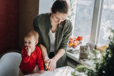 Mutlu anne ve küçük bebek bebek mutfakta noel kurabiyesi yapıp hamurla oynuyorlar. Anne ve küçük kız Noel arifesinde aile yemeği için zencefilli çörek pişiriyorlar..