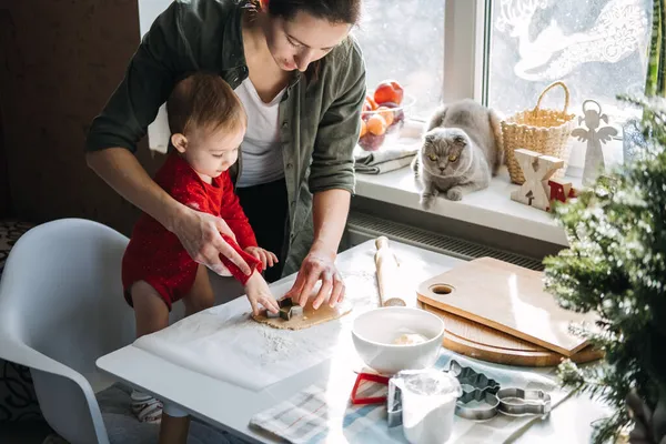 Happy mother and little baby toddler girl making christmas cookies in home kitchen and play with dough. Mother and little girl baking Christmas gingerbread pastry for family dinner on Xmas eve. — Stock Photo, Image