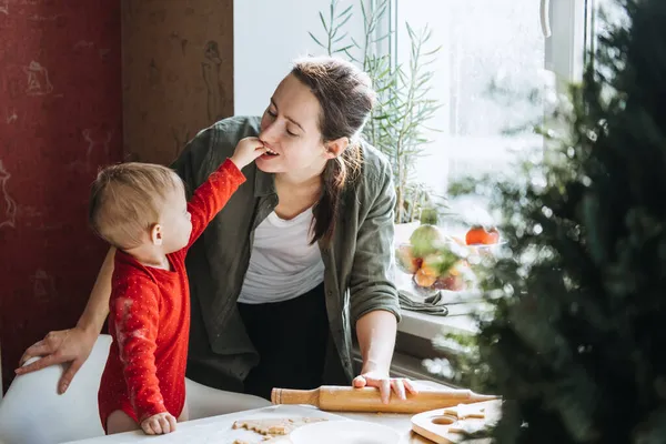 Glückliche Mutter und kleines Baby-Mädchen backen Weihnachtsplätzchen in der heimischen Küche und spielen mit Teig. Mutter und kleines Mädchen backen Weihnachts-Lebkuchen für das Familienessen an Heiligabend. — Stockfoto