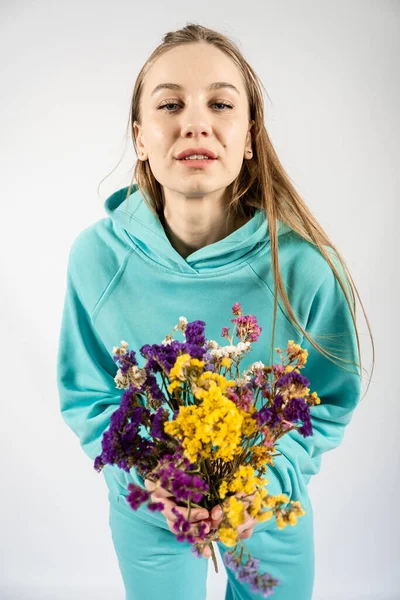 Retrato emocional sincero inalterado de jovem loira feliz mulher de cabelo longo com buquê de flores no fundo claro. — Fotografia de Stock