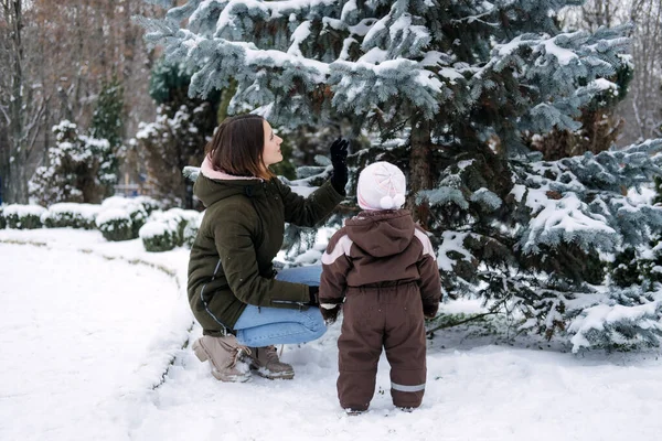 Zimowe spacery z niemowlętami i małymi dziećmi. Dziecko maluch w zimie, Jak chronić dzieci w zimnej pogodzie. Matka i córeczka spacerują po zimowym parku — Zdjęcie stockowe