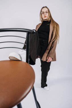 Heyecan verici genç bayan moda tasarımcısının stüdyo portresi, stilist. Şık, şık, uzun saçlı, rahat giyimli, sandalyeyle oynayan bir kız.