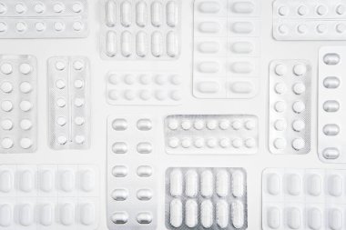 Beyaz haplar ve kapsül, beyaz arkaplanlı folyo paketinde ilaç tableti. Hapların ve kapsüllerin çeşitliliğiyle minimal geometrik tıbbi geçmiş.
