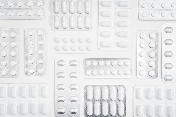 Białe tabletki i kapsułki, tabletki w blistrze foliowym z białym tłem. Minimalistyczne geometryczne tło medyczne z różnorodnością tabletek i kapsułek. — Zdjęcie stockowe