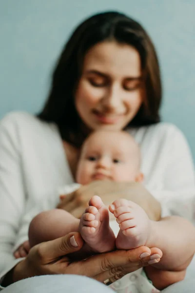 Медицинская страховка для новорожденных. Страхование жизни новорожденного. Мать держит в руках ноги новорожденного ребенка. Детские ноги в родительских руках — стоковое фото