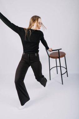 Heyecan verici genç bayan moda tasarımcısının stüdyo portresi, stilist. Şık, şık, uzun saçlı, rahat giyimli, sandalyeyle oynayan bir kız.