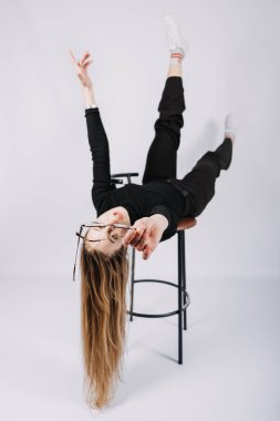 Heyecan verici genç bayan moda tasarımcısının stüdyo portresi, stilist. Şık, şık, uzun saçlı, rahat giyimli, sandalyeyle oynayan bir kız.