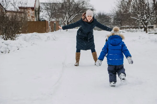 Rodzinne zajęcia na świeżym powietrzu na szczęśliwe ferie zimowe. Szczęśliwa matka i dwóch synów grających w śnieżki na śnieżnej ulicy na przedmieściach. Szczęśliwa rodzina na zimowy weekend, Święta Bożego Narodzenia — Zdjęcie stockowe
