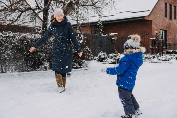 Rodzinne zajęcia na świeżym powietrzu na szczęśliwe ferie zimowe. Szczęśliwa matka i dwóch synów grających w śnieżki na śnieżnej ulicy na przedmieściach. Szczęśliwa rodzina na zimowy weekend, Święta Bożego Narodzenia — Zdjęcie stockowe