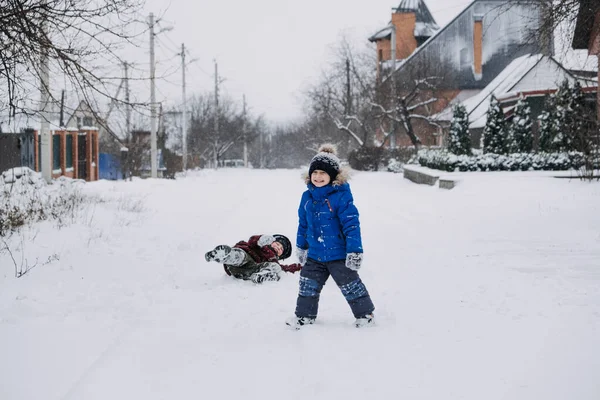 Zimowe zajęcia na świeżym powietrzu dla dzieci. Dzieci bawią się na przedmieściach, zbierają się na zimowym podwórku. Chłopcy, dwóch braci bawi się śniegiem. Skupienie selektywne — Zdjęcie stockowe