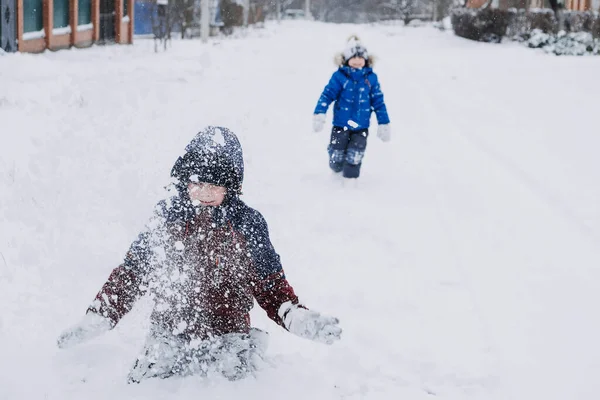 Zimowe zajęcia na świeżym powietrzu dla dzieci. Dzieci bawią się na przedmieściach, zbierają się na zimowym podwórku. Chłopcy, dwóch braci bawi się śniegiem. Skupienie selektywne — Zdjęcie stockowe