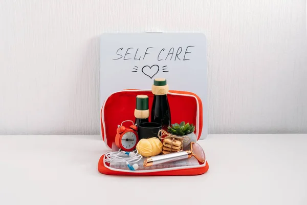 Self Care Kit, Self Care Package. Kosmetické láhve, masážní zařízení na obličej, sladkosti, sluchátka, vonné svíčky a tužky na barvu v červené lékárničce. Zařízení pro krásu, péči o sebe a volnočasové aktivity — Stock fotografie