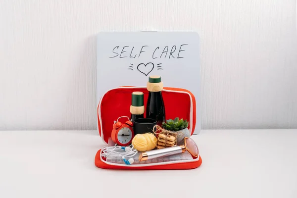 Self Care Kit, Self Care Package. Kosmetikflaschen, Gesichtsmassagegerät, Bonbons, Kopfhörer, Duftkerzen und Farbstifte für rote Verbandskästen. Geräte für Schönheit, Selbstpflege und Freizeitgestaltung — Stockfoto