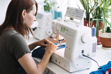 Tekrar kullan, onar, güncelle. Denim yükseltme fikirleri, tamir ve eski kot pantolon. Döküntü, eski, yırtık kot pantolon kumaşlı dikiş makinesinin yakın çekimi. Dikiş atölyesi çalışma süreci.