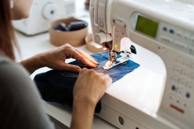 Tekrar kullan, onar, güncelle. Denim yükseltme fikirleri, tamir ve eski kot pantolon. Döküntü, eski, yırtık kot pantolon kumaşlı dikiş makinesinin yakın çekimi. Dikiş atölyesi çalışma süreci.
