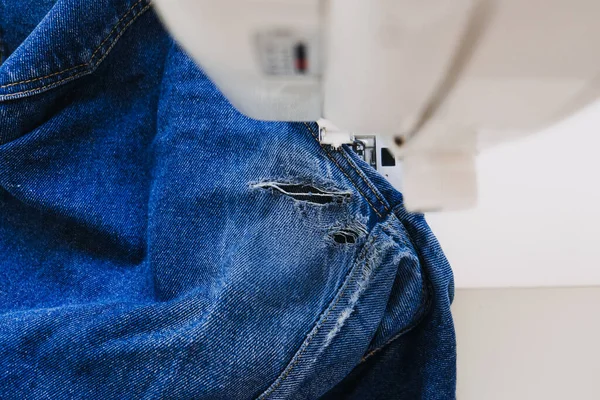 Reutilização, reparação, upcycle. Denim upcycling ideias, reparar e usar jeans velhos. Close-up da máquina de costura com tecido de jeans jeans rasgado, velho e esfarrapado. Processo de trabalho do estúdio de costura. — Fotografia de Stock