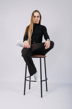 Stüdyo, sandalyede oturan uzun saçlı genç sarışın kadının değiştirilmemiş portresi. Havalı, şık, uzun saçlı, sıradan giyimli bir kızın portresi..