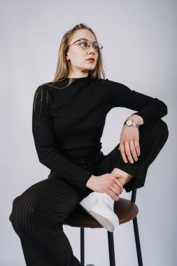 Stüdyo, sandalyede oturan uzun saçlı genç sarışın kadının değiştirilmemiş portresi. Havalı, şık, uzun saçlı, sıradan giyimli bir kızın portresi..