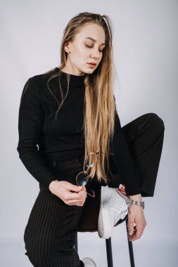 Stüdyo, sandalyede oturan uzun saçlı genç sarışın kadının değiştirilmemiş portresi. Havalı, şık, uzun saçlı, sıradan giyimli bir kızın portresi..