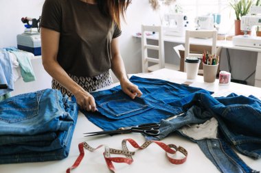 Sürdürülebilir moda, Denim Upcycle Fikirleri, Eski Kotları Kullanmak, Kotları Yenilemek, Eski Kotları Yeniden Kullanmak, Upcycle Stuff. Kadın terzi dikiş atölyesinde eski kot pantolonları kesip onarıyor.