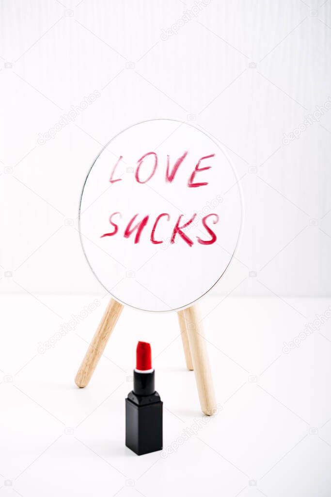 Loneliness, Broken heart, Divorce, couple breakup and relationship family breakdown concept with red lipstick text Love Sucks on mirror, glasses of rose wine on table.