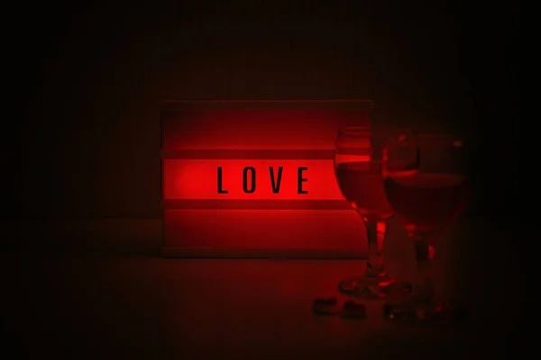 Ideas for Romantic Date Night at Home. Valentines Day quotes. Valentine Day, romance, dating concept. Red lightbox with word Love and two glasses of wine in evening. — Stock Photo, Image