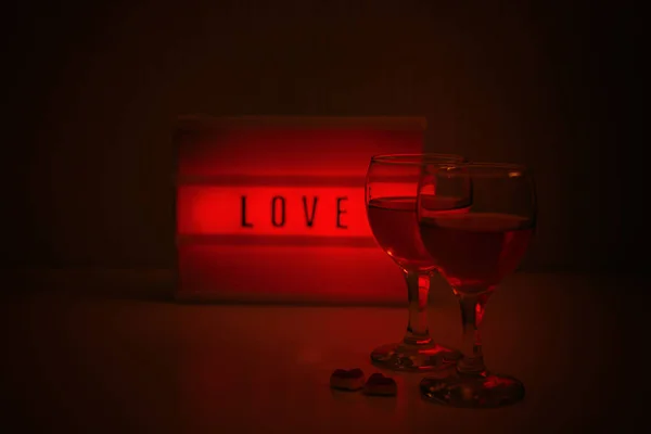 Ideas for Romantic Date Night at Home. Valentines Day quotes. Valentine Day, romance, dating concept. Red lightbox with word Love and two glasses of wine in evening. — Stock Photo, Image