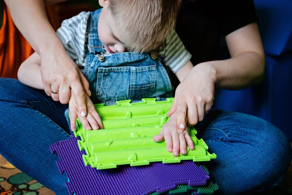 Sinnesspiele für Kinder mit besonderen Bedürfnissen. Hilfe und Aktivitäten für Kinder mit Behinderungen, Zerebralparese. Junge mit Zerebralparese spielt mit Sinnesmatten-Massage-Spiel Puzzlematten für Kinder — Stockfoto