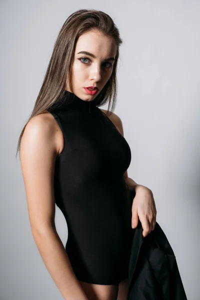 Retrato de estudio de una joven con el pelo largo. Chica con estilo de moda en traje de cuerpo negro sobre fondo gris —  Fotos de Stock