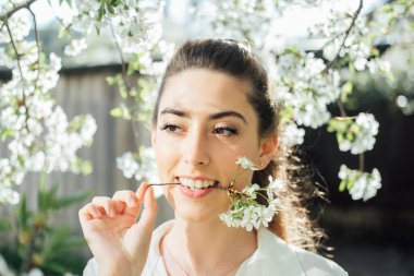 Bahar geliyor. Doğal güzellik. Bahar bahçesinde beyaz çiçeklerin arasında güzel genç bir kadın. Çiçek açan bahar bahçesinde kokunun tadını çıkaran genç bir kadın.