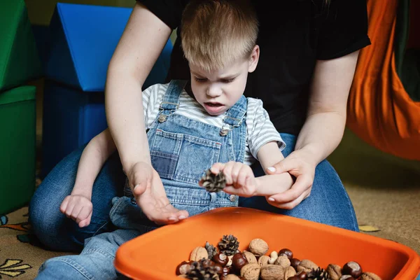 Sinnesspiele für Kinder mit besonderen Bedürfnissen. Hilfe und Aktivitäten für Kinder mit Behinderungen, Zerebralparese. Junge mit Zerebralparese spielt mit Naturmaterialien Zapfen und Nüsse — Stockfoto